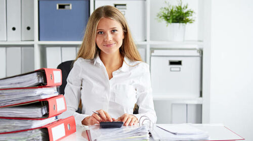 Smiling business woman calculates tax at desk in office