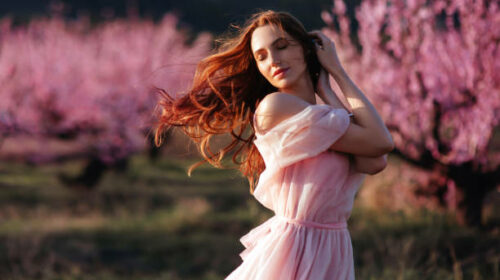 Beautiful young girl under the flowering pink spring tree