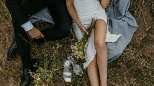 Groom and bride sitting in grass on a meadow in nature.