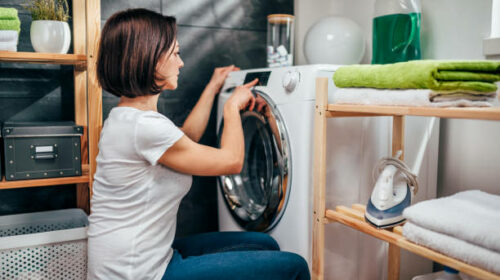 Woman wearing white shirt choosing program on washing machine in laundry room