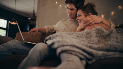 Young,Couple,Sitting,On,Sofa,At,Home,In,Winter,And