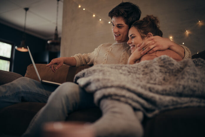 Young,Couple,Sitting,On,Sofa,At,Home,In,Winter,And